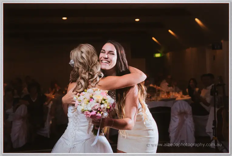 A guest in a cream dress hugs Cristina beaming, clutching the just-caught pink and cream bouquet