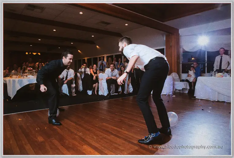 Two men crouch warily over balloons on the dance floor as guests film the standoff