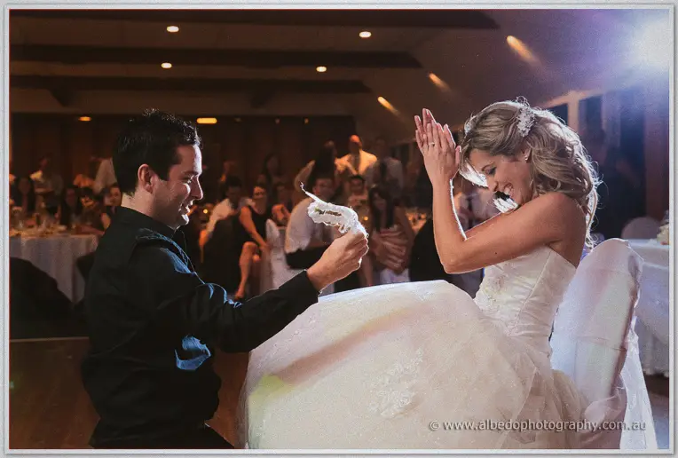 The groomsman waves the lace garter aloft while Cristina laughs, hands raised, beside him