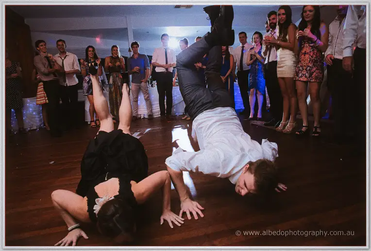 Wedding guests do breakdancing floor moves on the dance floor while a cheering crowd watches