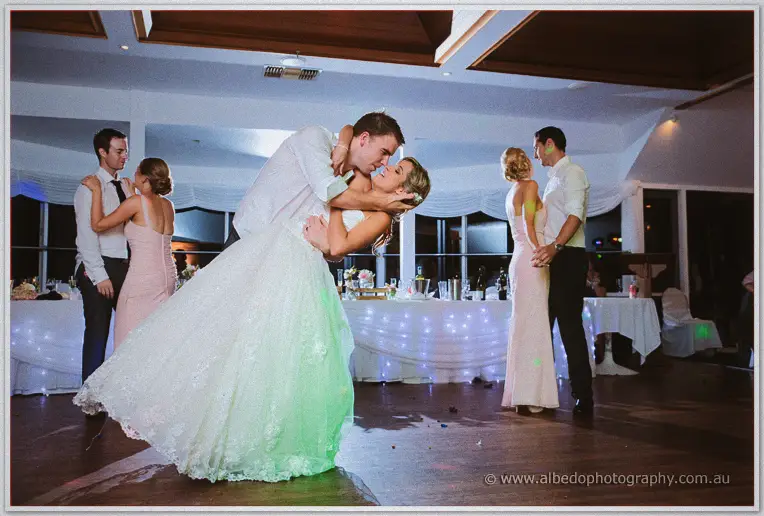 Bride and groom share a deep dip beside couples swaying near fairy-lit tables at the yacht club