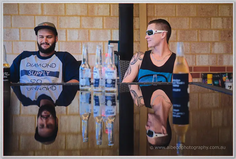 Groomsmen relax over drinks on the patio, mirrored in the glossy black table on a sunny morning.