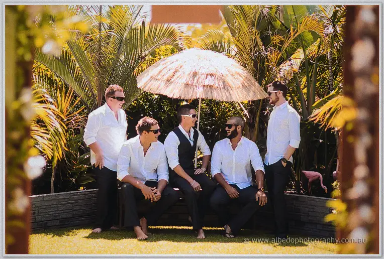 Shane and his groomsmen laze barefoot under a thatched umbrella in the lush tropical backyard.