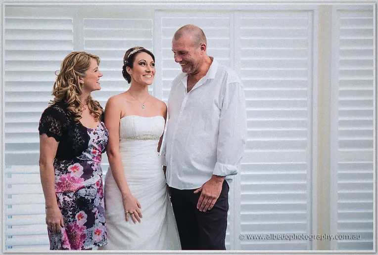 Elisha stands between her smiling parents in a bright room for a family portrait