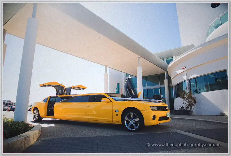 A yellow stretch limousine waits with its doors open beneath a modern white canopy
