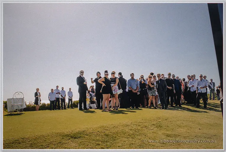 Guests gathered on a sunlit lawn awaiting the ceremony at the golf course