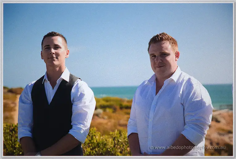 Two groomsmen wait before the ocean backdrop during the outdoor ceremony