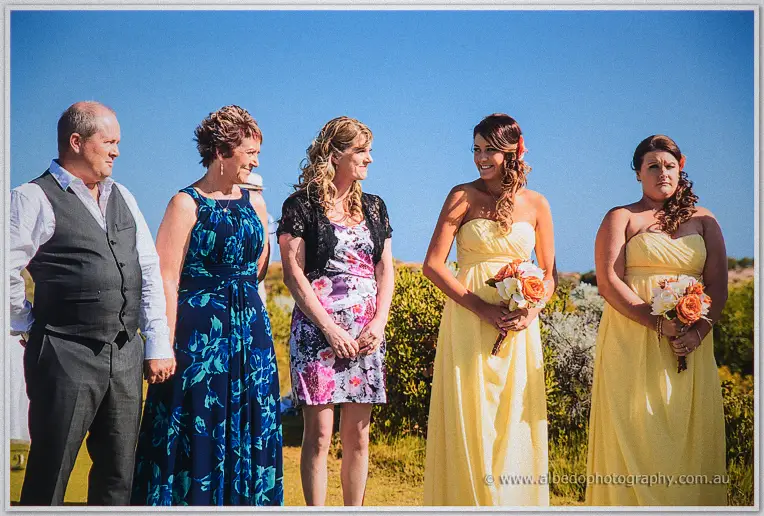 Bridesmaids hold their bouquets as family look on under the bright ceremony sky