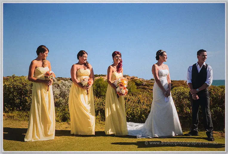 Bridesmaids in yellow stand with Elisha and Shane before the coastal ceremony backdrop