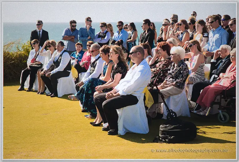 Guests seated in white covers watch the ceremony against the turquoise sea