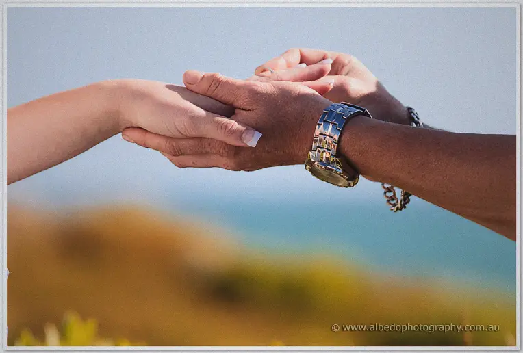 Tight crop of the newlyweds' clasped hands with the ocean blurred behind