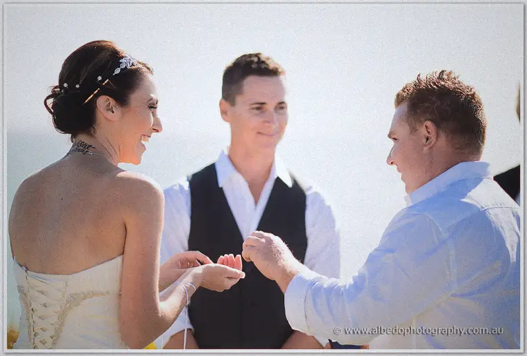 A groomsman hands over the ring while Elisha laughs and Shane watches