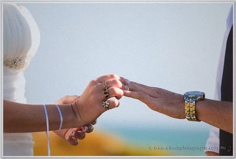 Macro of hands during the ring exchange with turquoise water beyond