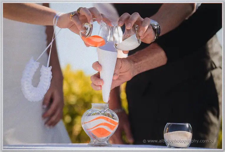 Elisha and Shane pour orange and white sand into a heart-shaped glass vase