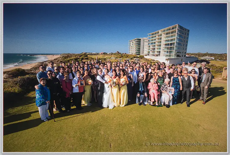 Whole guest group photo on the green with beach and apartment towers behind