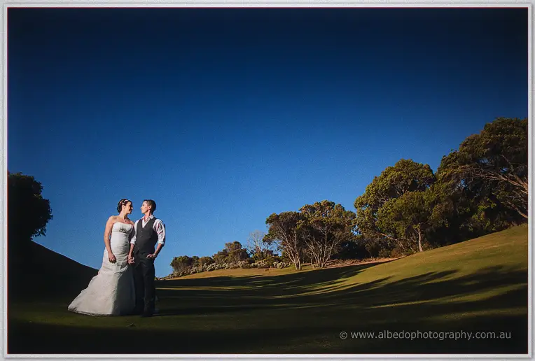 Elisha and Shane stand close on the fairway at dusk, deep blue sky over the trees at The Cut