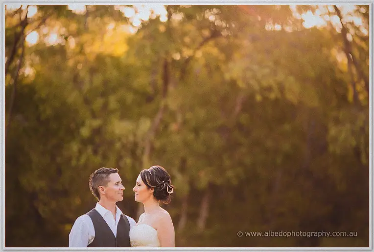Elisha and Shane gaze at each other in warm golden light, soft trees glowing behind them