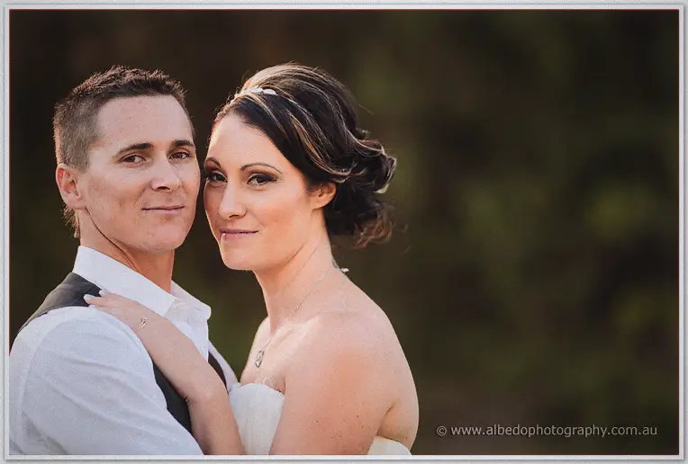 Close portrait of Shane and Elisha cheek to cheek, her updo and headpiece catching the soft evening light