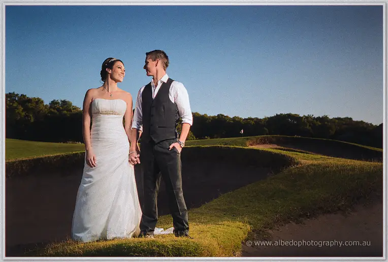 Couple hand in hand on the bunker's edge, golden light and deep blue sky over the golf course