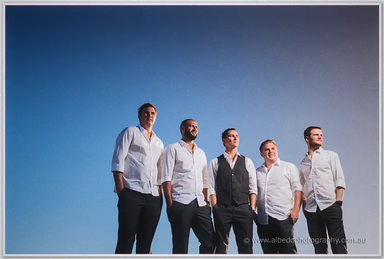 Shane and his groomsmen laugh together on the ridge, low angle against the wide blue sky