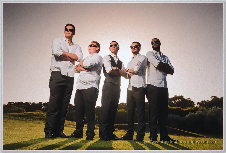 Shane and groomsmen strike poses in sunglasses on the green, long shadows and bright backlight