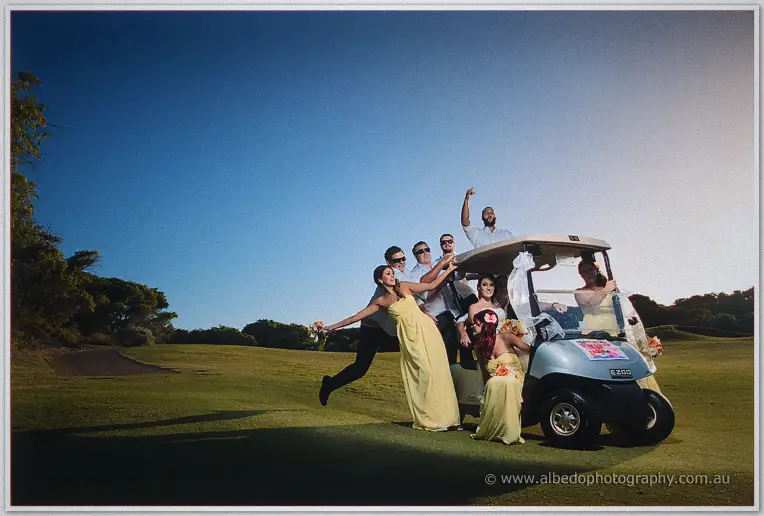 Bridal party in yellow gowns piles around a decorated golf cart on the course at dusk