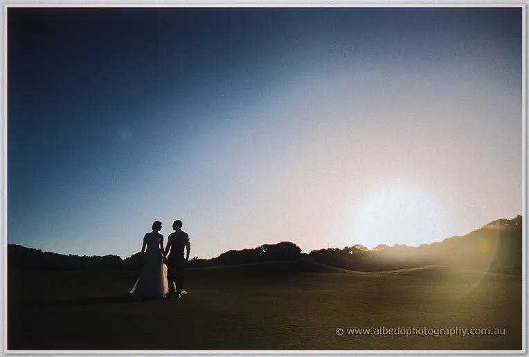 Elisha and Shane walk hand in hand into the sunset haze across the golf course