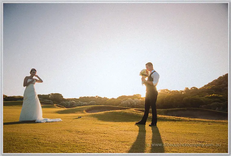 Shane holds the bouquet while Elisha laughs from across the green in warm evening light