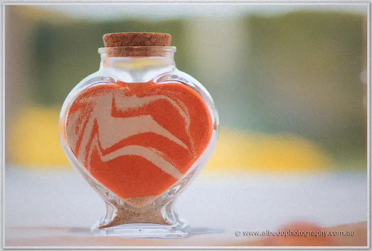 Heart-shaped corked jar holds swirled orange and white sand from the ceremony ritual