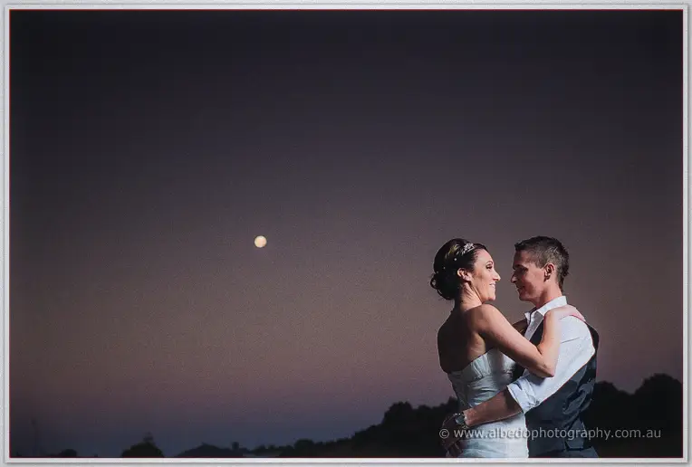 Elisha and Shane embrace under a full moon rising in the violet dusk sky