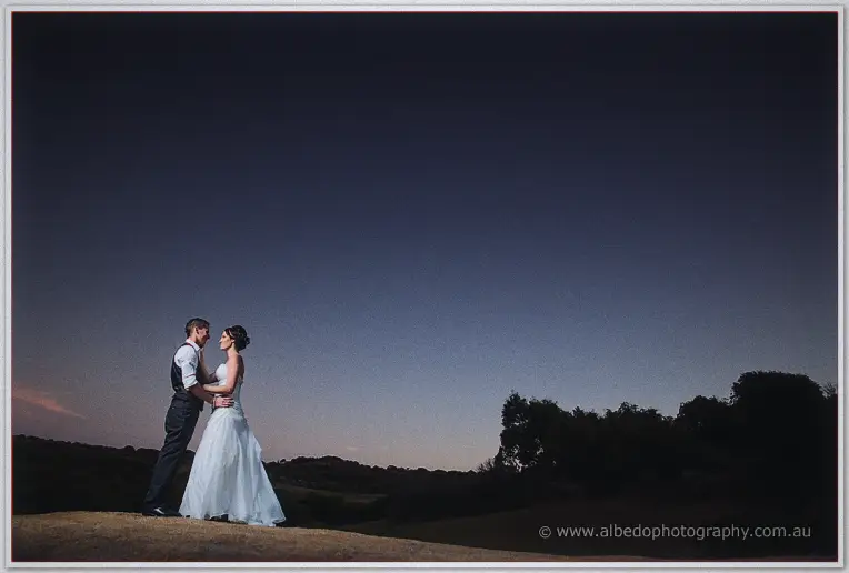 The couple stands forehead to forehead on a rise beneath a vast indigo evening sky