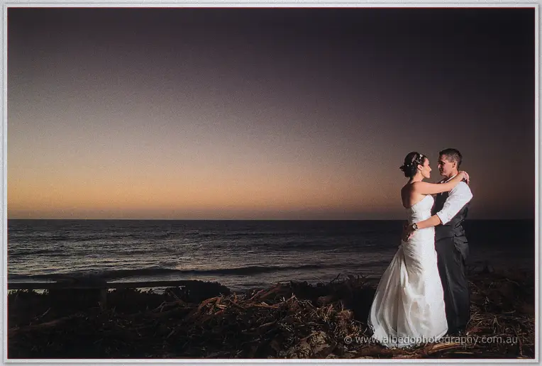 Bride and groom hold each other on the dunes as dusk settles over the ocean