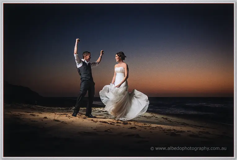 Shane throws both fists in the air as Elisha spins her gown at nightfall on the beach