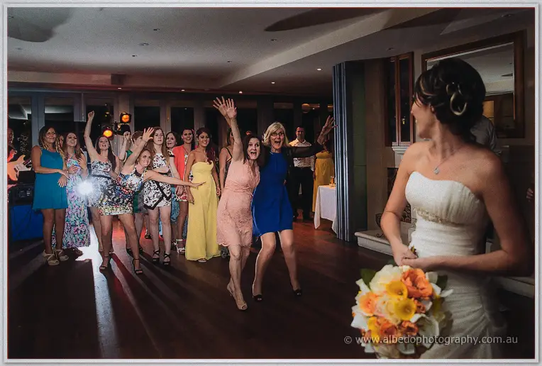 Women reach skyward as Elisha turns to toss her orange and yellow bouquet across the dance floor