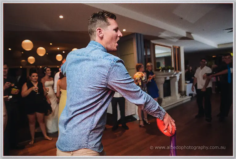 A groomsman flings the garter football over his shoulder under paper lanterns as wedding guests watch on