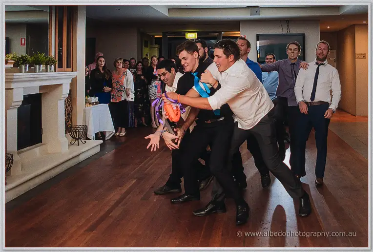 Men in shirts and ties lunge for the tossed garter football on the dance floor as guests watch