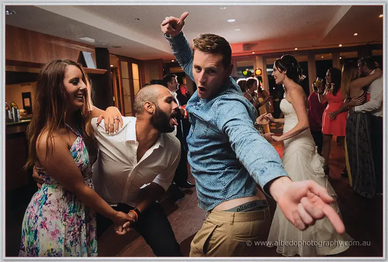 Three friends ham it up mid-dance, the bearded one tongue out, while the bride laughs in the background