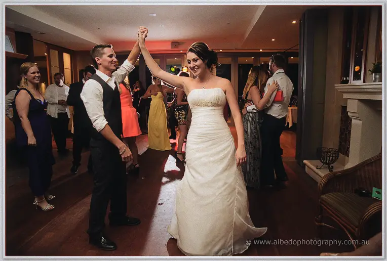 The groom spins his strapless-gowned bride across the dance floor under warm reception lights