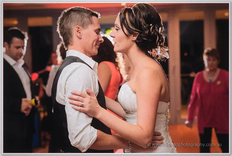 The bride rests a hand on her groom's chest as they sway close in soft evening light