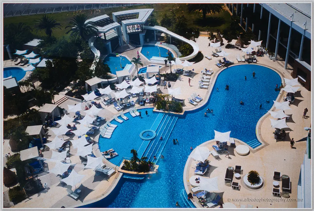 High overhead view of the resort pool deck, white shade sails scattered across turquoise water