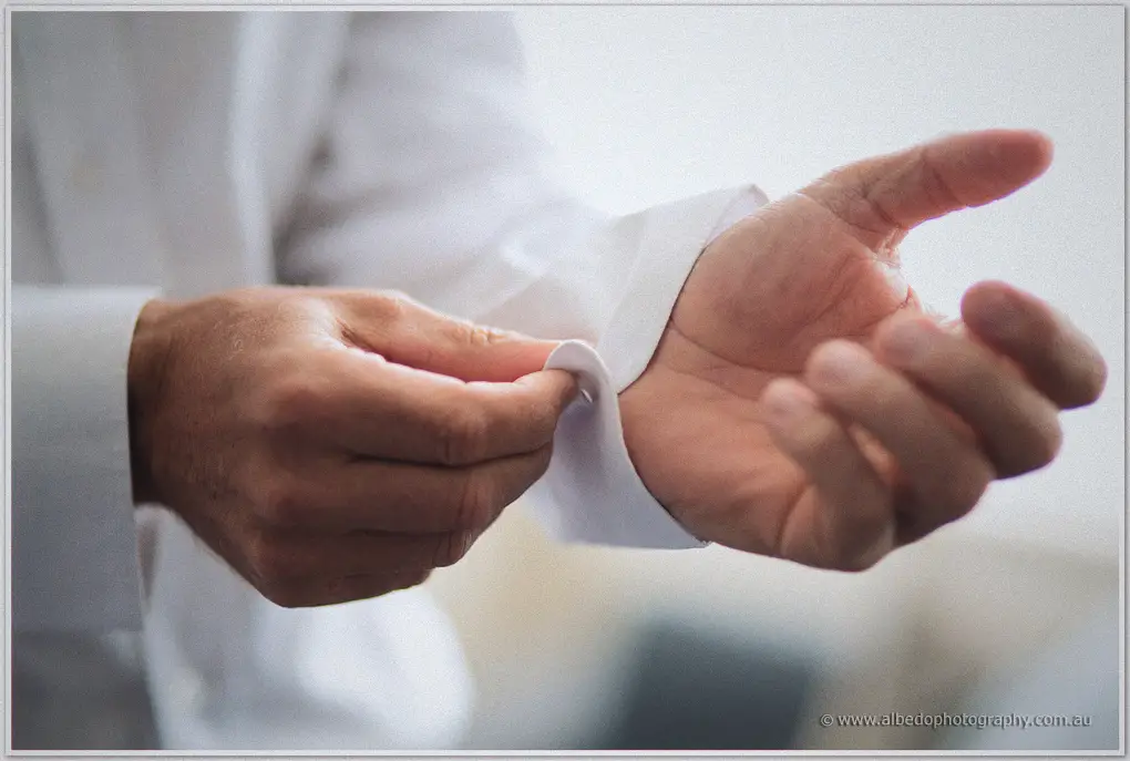 Close-up of fingers fastening a cufflink through a crisp white shirt cuff