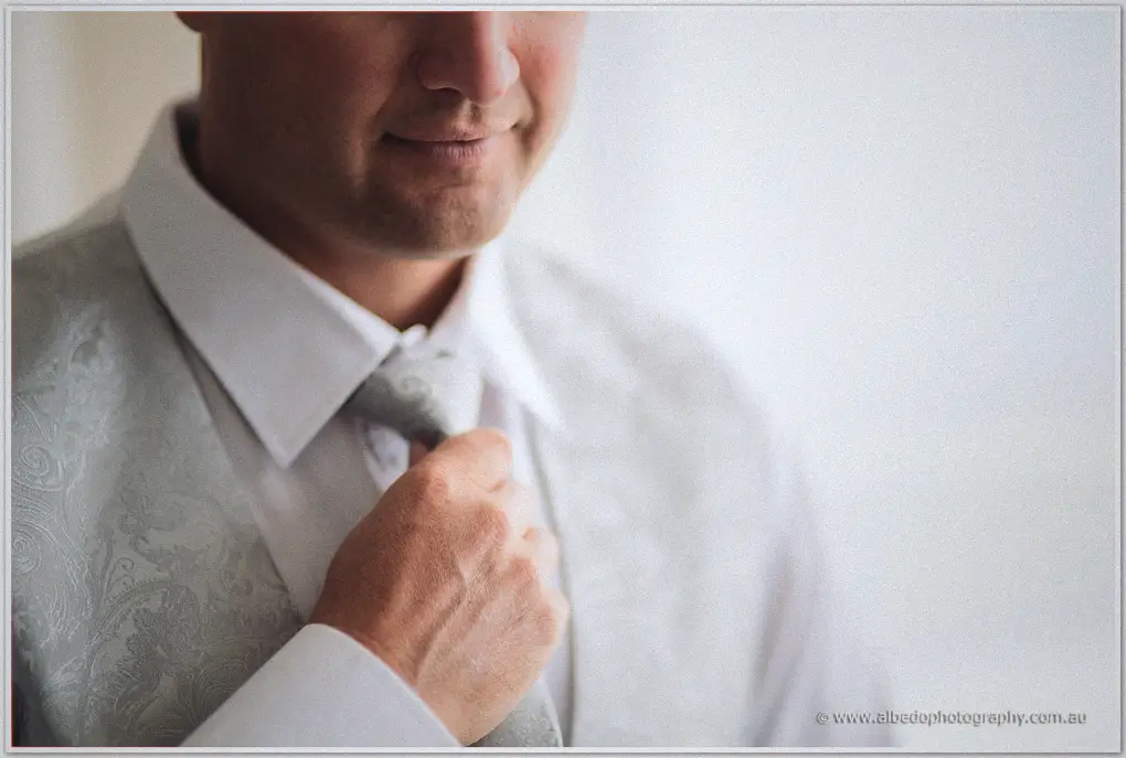 Close-up of Ashley in a paisley waistcoat tugging his silver tie into place