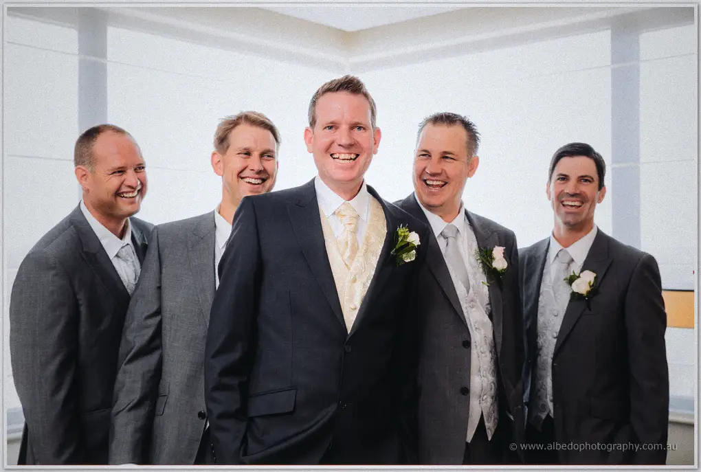 Ashley grins at the centre of his four laughing groomsmen, white boutonnieres pinned