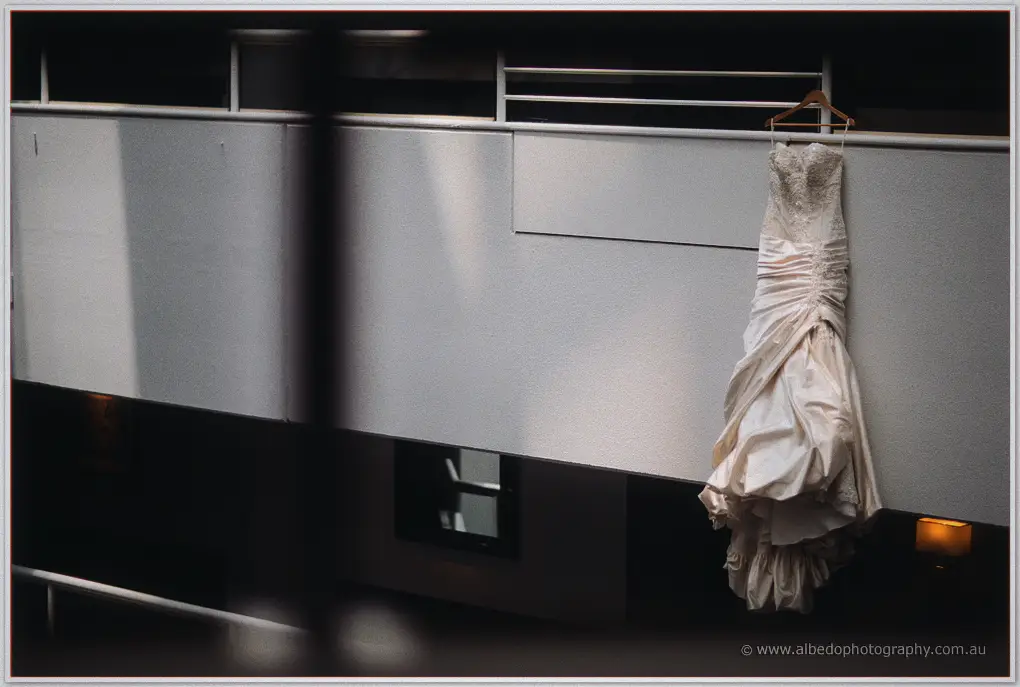 Kristina's ruched mermaid gown hangs from a loft rail in dramatic shafts of light