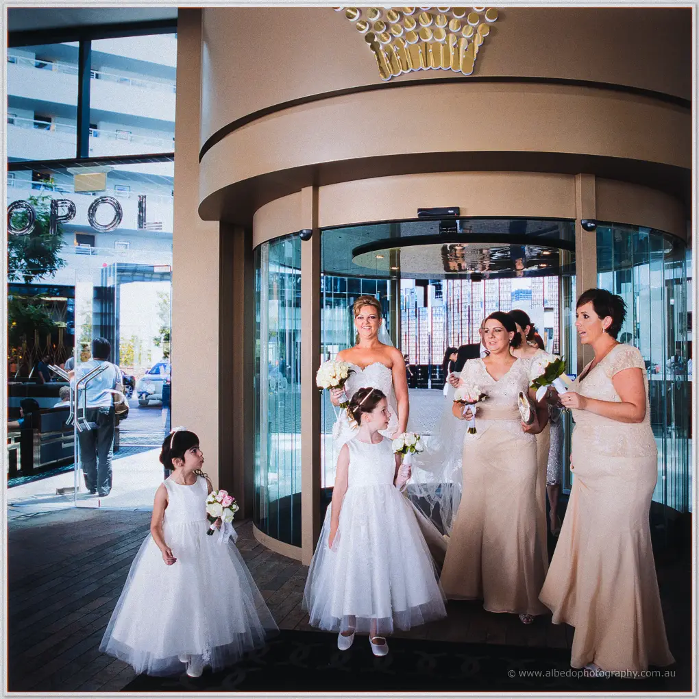 Kristina and her bridal party file through hotel revolving doors with two flower girls
