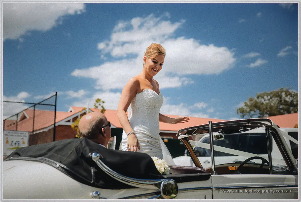 Kristina rises laughing from the convertible's back seat against a bright, clouded sky