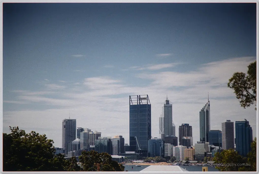 Perth's glass towers rise over the Swan River beneath a wide, cloud-washed sky