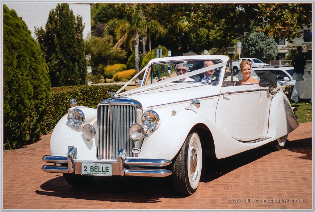 Kristina rides up a red-brick drive in a ribbon-trimmed Jaguar convertible with her father driving