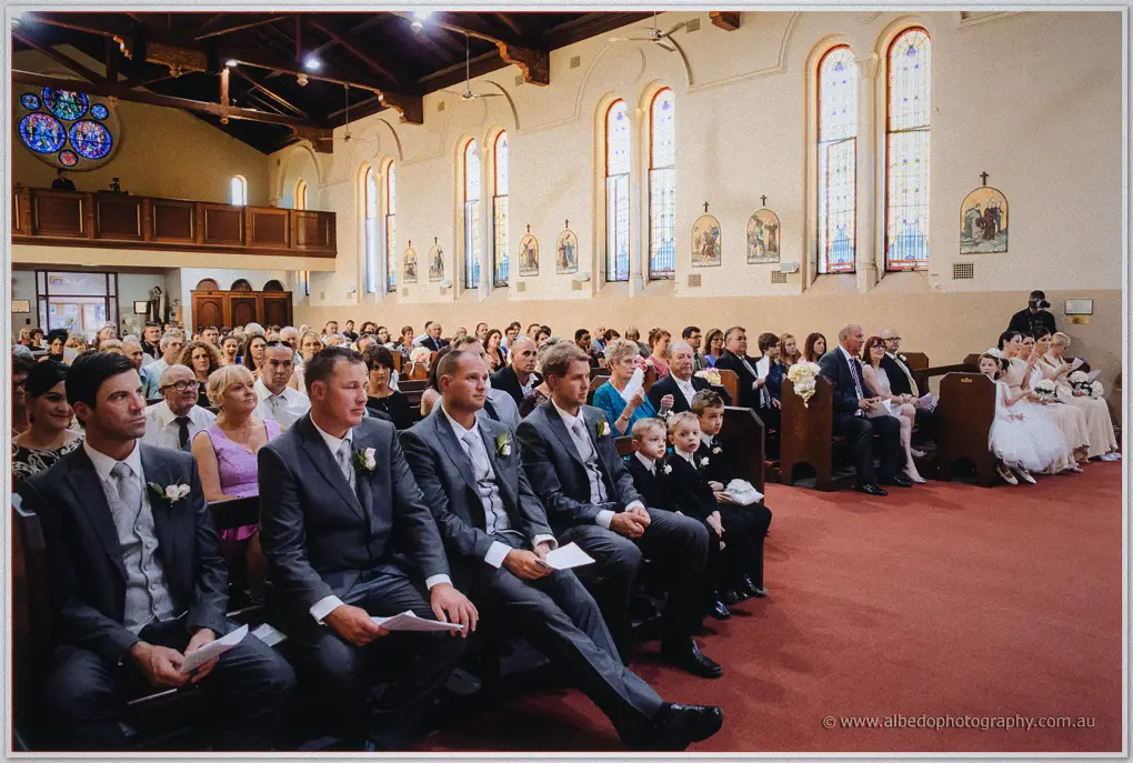 Groomsmen and page boys fill the front pew beneath arched stained-glass windows