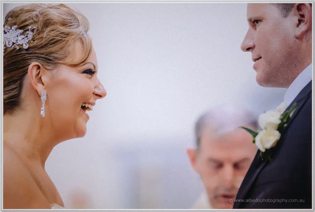 Tight profile of a beaming Kristina facing Ashley, the priest blurred between them